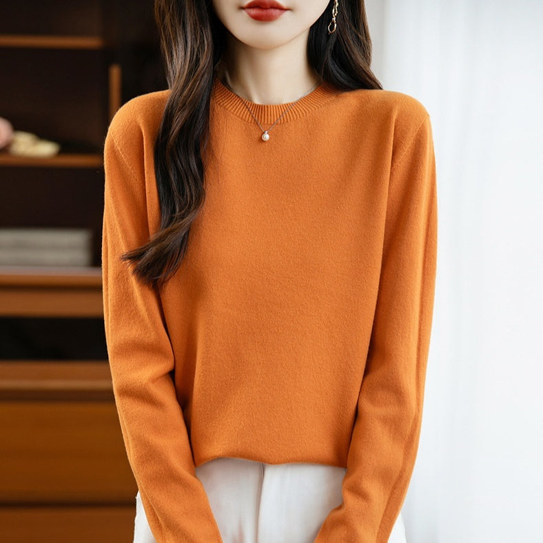 Woman wearing a seamless round-neck wool knit pullover sweater in soft natural light, knit texture visible against a neutral wool-toned backdrop